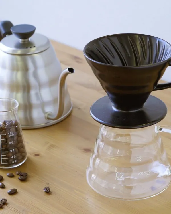 A dark V60 dripper on a glass server, next to a kettle
